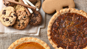 Rustic brown table with four different kinds of holiday desserts: cookies, gingerbread men, pecan pie, and pumpkin pie all on the table.