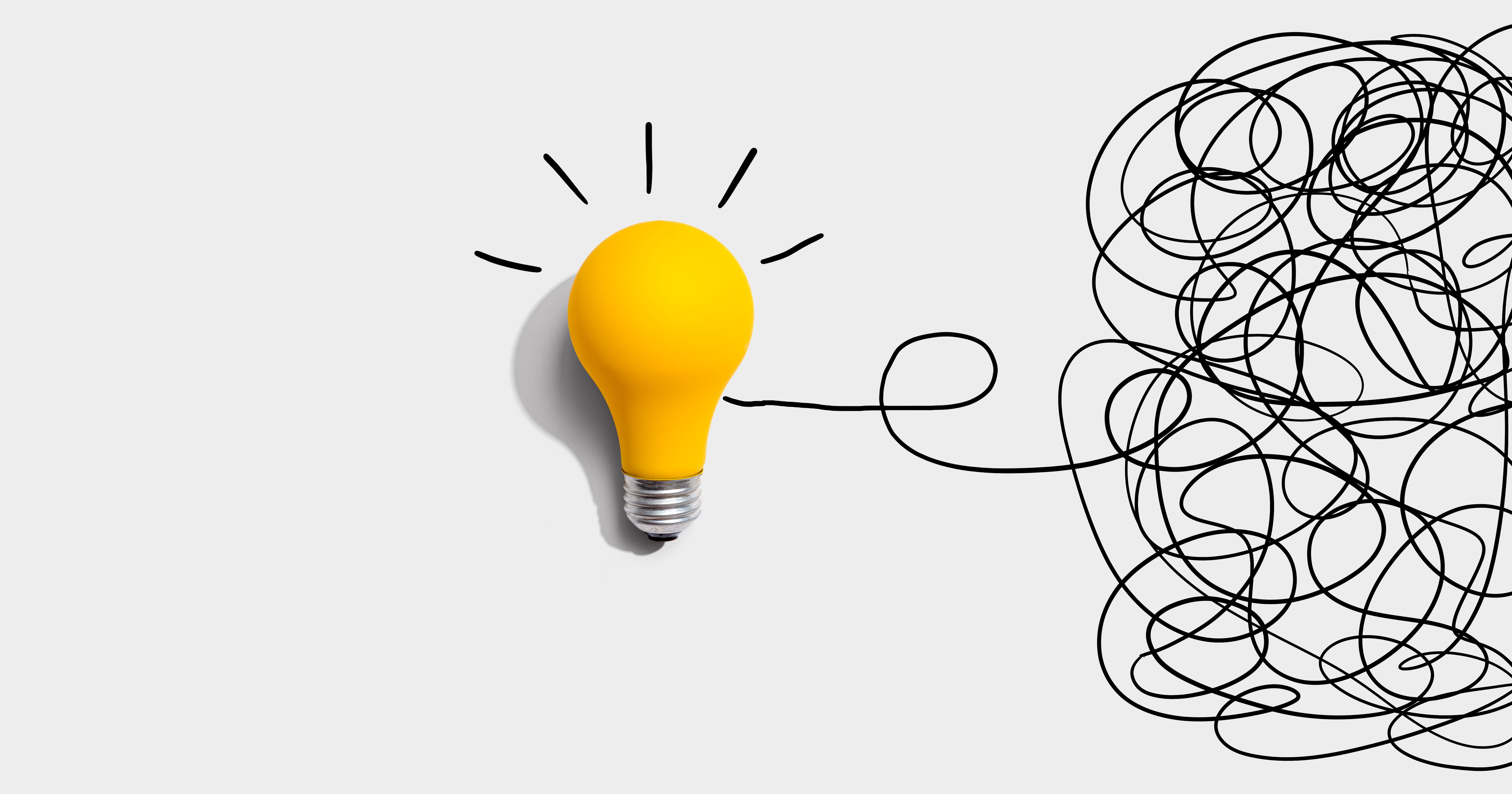 Clarifying complex ideas theme with yellow light bulb emerging from a pile of black scribbles on a white background.